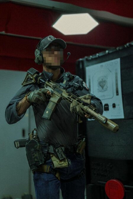 Operator in helmet and plate carrier shouldering a rifle at an indoor range